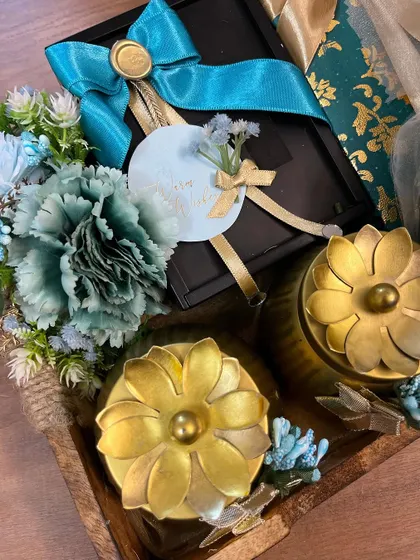 A close-up of the details in the teal and gold wedding hamper, including the floral-lidded jars and a large satin bow with a wax seal.