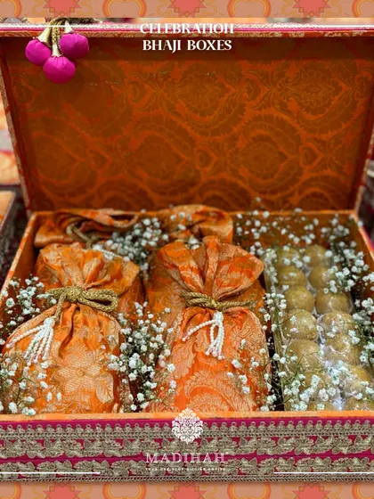 My Celebration Bhaji Boxes are designed to spread joy. This ornate box, in a vibrant orange and pink brocade, is filled with traditional sweets and potlis, perfect for any festive occasion.
