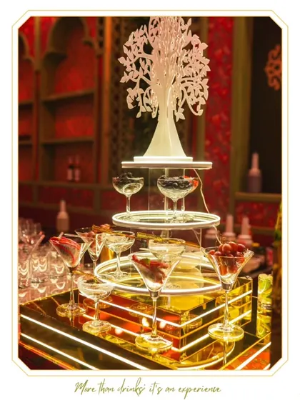 This elegant bar setup uses a tiered, illuminated display and a decorative tree centerpiece to create a visually stunning focal point. The design combines modern lighting with classic elegance for a luxurious feel.