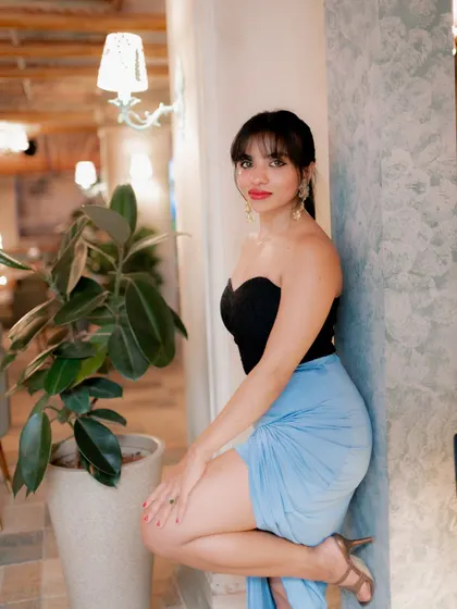 A stylish indoor portrait. The model's pose against the wall and the soft ambient light create a chic and relaxed lifestyle shot.