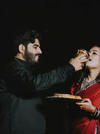 The gentle act of breaking the fast. This photo captures the husband feeding his wife, a tender and significant ritual of Karwa Chauth, framed against the dark night for a powerful, focused effect.