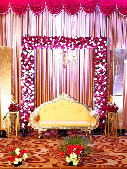 This wedding reception stage combines classic and modern elements with a floral arch set against shimmering gold and pink curtains. I used geometric gold frames and chandeliers to add a touch of regal elegance to the decor.