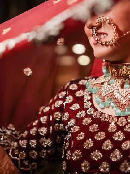 A close-up, artistic shot focusing on the bride's jewelry and the edge of her veil. The details of her velvet lehenga and the turquoise in her necklace are beautifully highlighted.