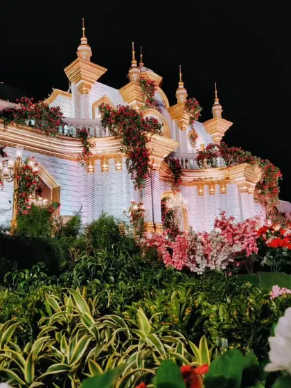 A low-angle view of the palace facade, emphasizing the lush greenery and floral arrangements at its base, which contrast beautifully with the white and gold structure.