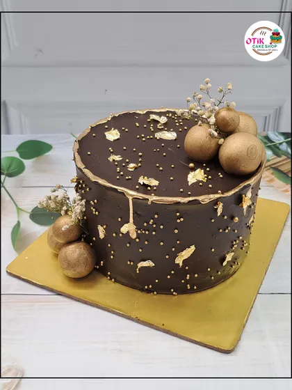 A sophisticated take on a chocolate cake. This design features a smooth chocolate ganache, gold leaf flakes, and golden chocolate spheres for a touch of elegance.