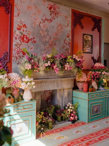 A stunning vignette featuring a faux fireplace overflowing with flowers, set against a wall with a beautiful floral mural. This creates a cozy and incredibly romantic focal point.