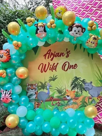 A "Wild One" jungle-themed birthday party with a circular backdrop. The decoration features a green and gold balloon arch and animal foil balloons.