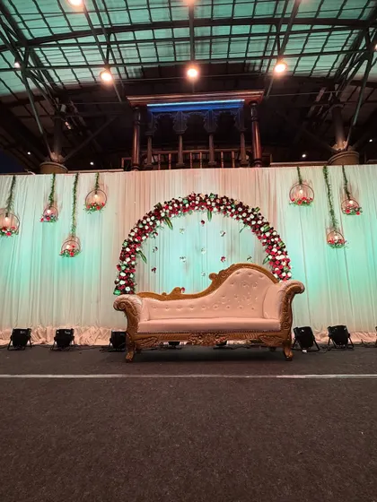 A simple yet elegant engagement stage with a floral half-arch and a classic chaise lounge. Perfect for intimate celebrations.