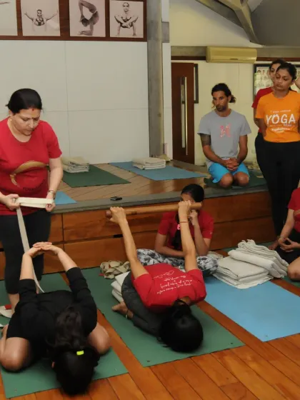 I am demonstrating the use of a belt to help students in a seated forward bend. The belt acts as an extension of the arms, allowing for a deeper and more controlled stretch.