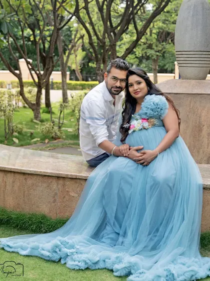 A beautiful portrait of the couple seated on a stone bench in a lush garden. The flowing blue gown adds a touch of fairytale magic to the natural setting.