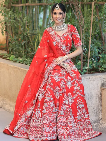 A smiling bride seated in an elegant red lehenga with silver embroidery, paired with a matching diamond and pearl necklace set.