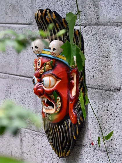 A side view of the Bhairava mask, showing the three-dimensional carving and the way it interacts with the surrounding foliage. These masks are an important part of Nepalese culture, meant to be displayed in living spaces.