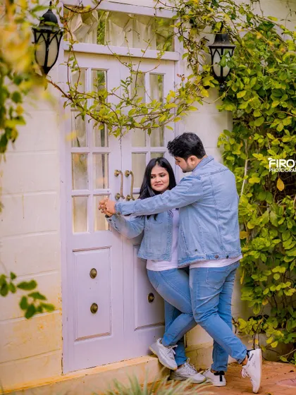 A fun, dancing pose in front of a white door, framed by green vines. The couple's matching denim outfits and their joyful interaction make this a great shot.