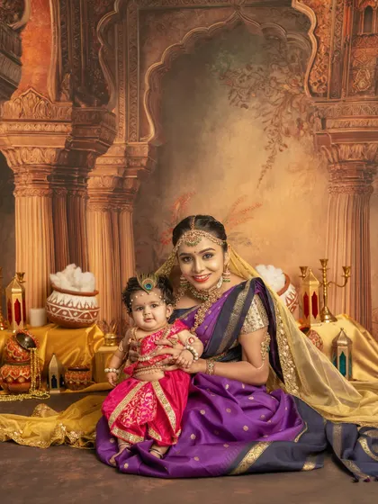 A stunning portrait of a mother and her baby girl dressed as Krishna. The rich, traditional backdrop and their coordinated outfits create a regal and timeless image for Janmashtami.