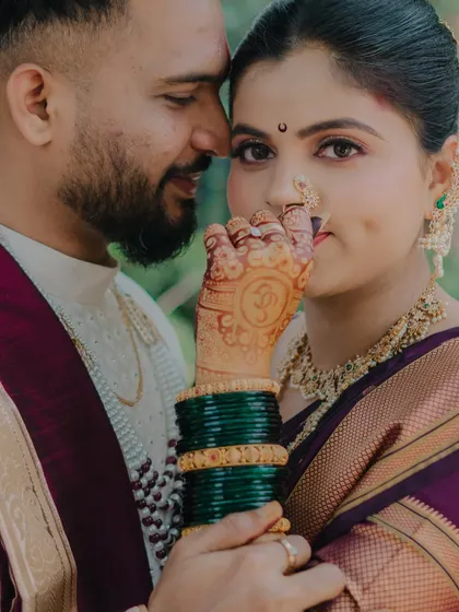 A detailed close-up focusing on the bride's henna-adorned hand, her traditional nath, and the loving gaze of her groom.