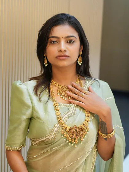 Sonu trying on a traditional gold necklace that beautifully complements our custom-designed saree and blouse.