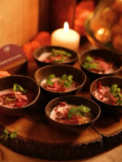 A rustic wooden platter holding bowls of a vibrant pink soup, garnished with fresh herbs. The warm, candlelit ambiance makes this an inviting shot for a cozy, festive dinner.