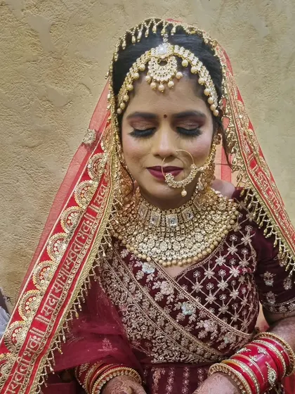 A close-up portrait of the bride. The makeup is flawless, with a focus on a strong base and well-defined features to complement her heavy bridal jewelry.
