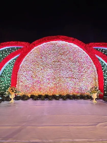 This reception stage is a celebration of color, with massive arches covered in red and multi-colored flowers. The design creates a dramatic and festive backdrop for a grand celebration.