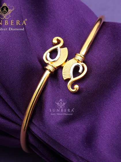 An elegant gold open-cuff bracelet with paisley-shaped terminals in a two-tone finish. This design blends traditional motifs with modern style, making it a versatile accessory.
