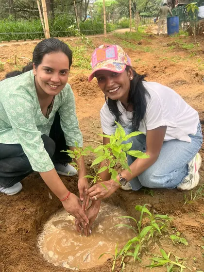 Two smiling volunteers from Infoglen plant a native sapling together, contributing to our goal of planting one million trees in Gurgaon.
