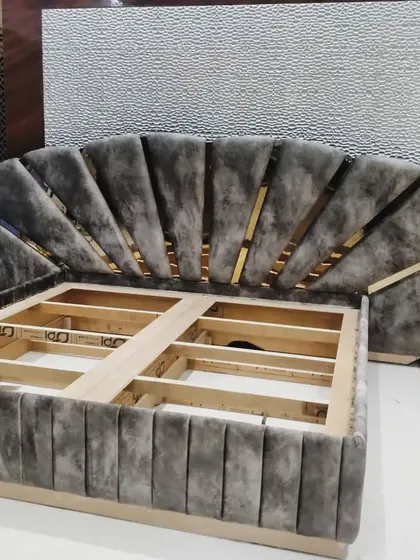 The bare frame of another custom bed, showing the solid wood construction and the unique fan-shaped headboard design with grooves for metal inlays.