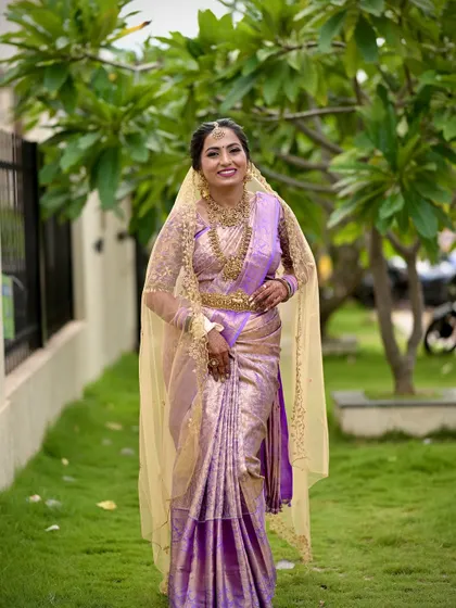 This bride looks regal in her lavender silk saree and gold veil. Her makeup is glamorous, with a focus on defined eyes and a perfectly matching lip color.