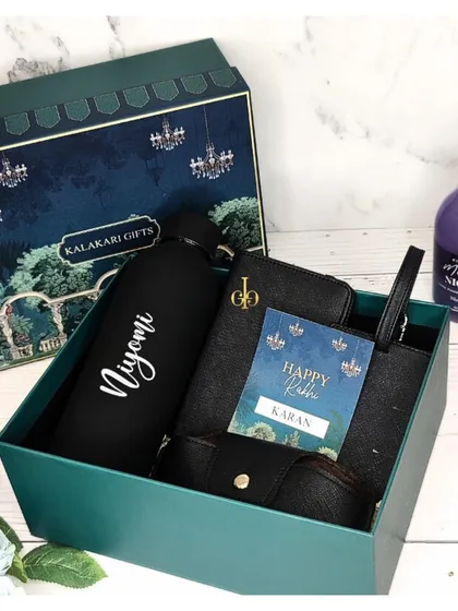 A sleek and modern Rakhi hamper for him in a black and green theme. It includes a personalized water bottle, a matching travel accessories set, and a "Happy Rakhi" card.