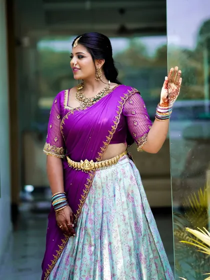 This ensemble was created by repurposing a beautiful silk saree into a flowing skirt. I paired it with a contrasting purple dupatta and an embroidered blouse with sheer sleeves, creating a vibrant and unique half-saree style lehenga.