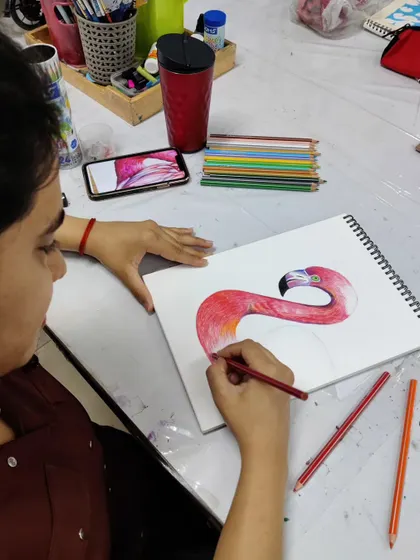 Another angle of the student working on her flamingo drawing, showing the layering of different shades of red and pink to build up color depth.