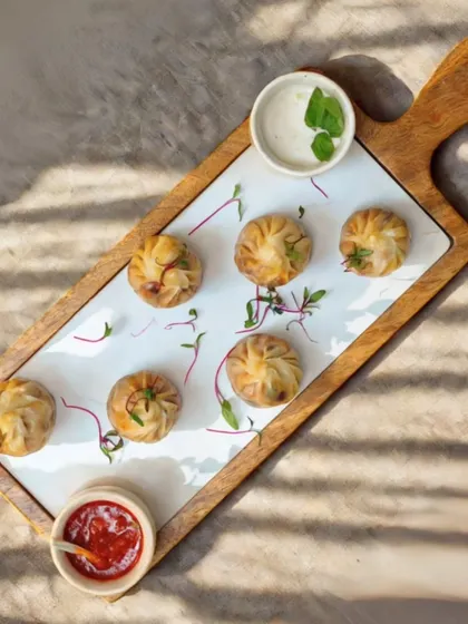 A platter of perfectly steamed momos, presented on a modern wooden and white board with two dipping sauces. Simple, elegant, and always a crowd pleaser.