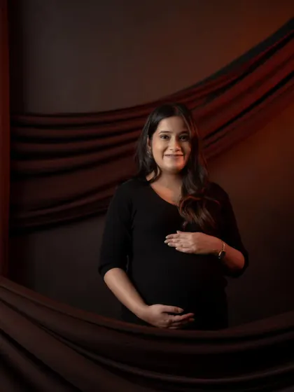 A classic portrait against a dark, draped backdrop. The simple setup and direct gaze create a powerful and confident image of the mother-to-be.