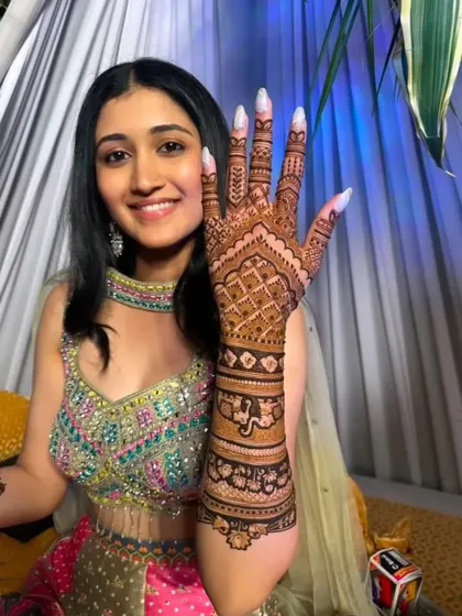 A happy bride showing her palm, covered in a beautiful jaali pattern. The intricate design and her bright smile are a perfect match.