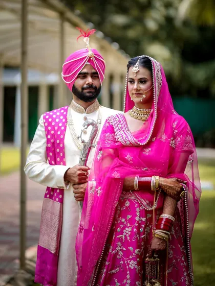 A classic portrait of a Punjabi bride and groom in their stunning wedding attire, holding a ceremonial sword.