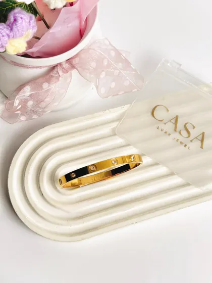 A single gold bangle placed on a textured tray. This minimalist approach draws all attention to the product, highlighting its classic design and finish.