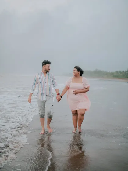 A couple walks hand-in-hand along the wet sand, creating beautiful reflections.