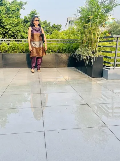 A newly made rooftop garden in GK, Delhi. Here I am, standing on the clean, tiled surface, with a border of freshly planted shrubs and palms in modern black planters.