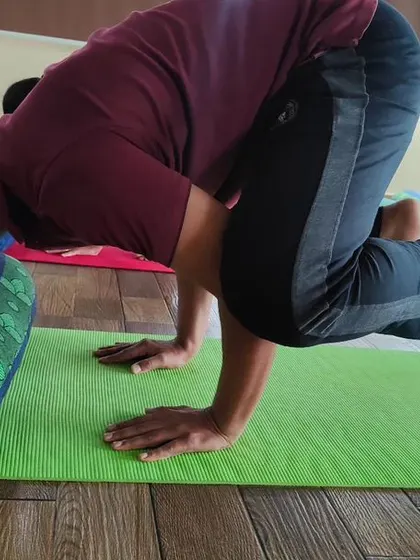 A student practices Kakkasana (Crow Pose) with a bolster for support. Using props is a smart way to understand the mechanics of an arm balance and build confidence before lifting off completely.