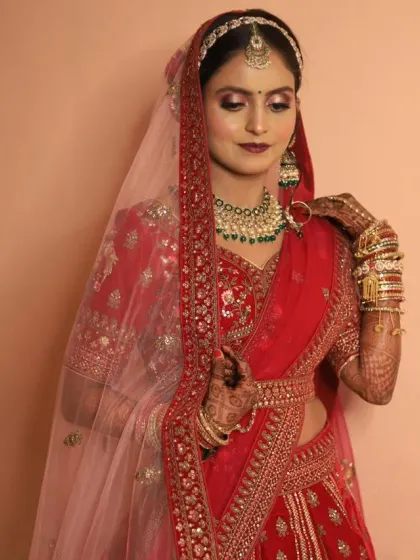 This bridal look features a beautiful red and green color combination. The hairstyle is a classic bun decorated with red roses and pearls, complementing her stunning lehenga.