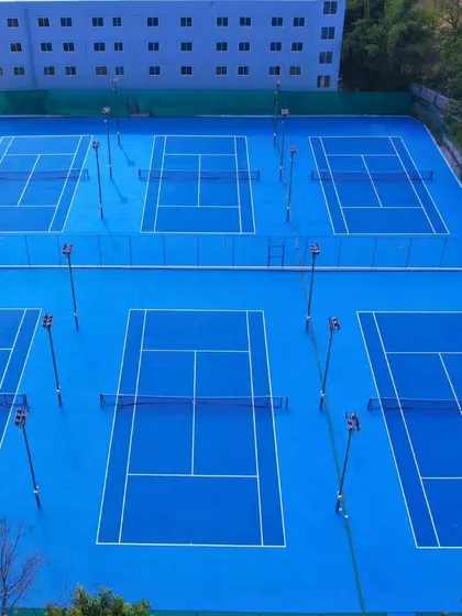 A stunning view of our six-court block, complete with floodlights for night sessions. The vibrant blue acrylic surfaces are maintained to international standards, providing the perfect stage for player development.