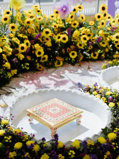 The traditional 'chowki' for the Haldi ritual, placed in a scalloped basin and surrounded by a dense ring of sunflowers and purple chrysanthemums.