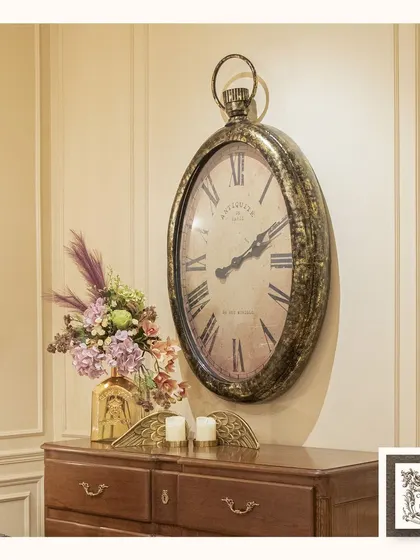 This large, oval wall clock is inspired by antique Parisian pocket watches. Its distressed metal finish and classic Roman numerals add a touch of vintage sophistication to this console table display.