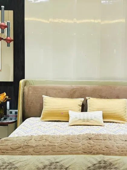 A close-up of a bedroom with a soft, brown upholstered bed and unique pendant lights. The wall art adds a touch of abstract texture to the serene space.