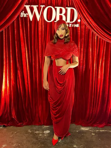 The full silhouette of the crimson cowl-drape set against a matching red backdrop, a look that is unapologetically bold.