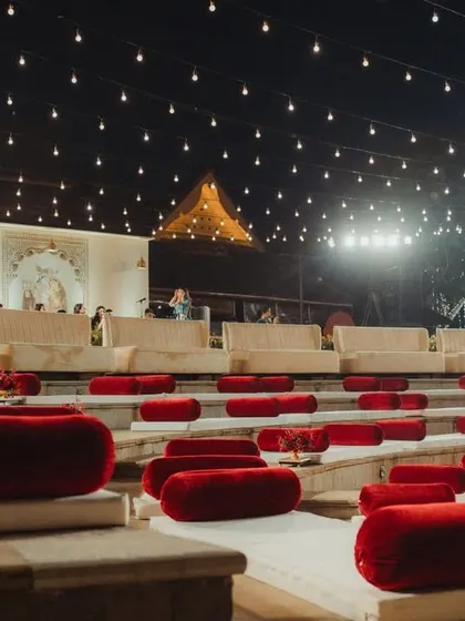 The amphitheater seating arranged for the wedding ceremony, with plush red velvet cushions on the stone steps. This setup provides guests with a clear, comfortable view of the grand mandap under the open night sky.