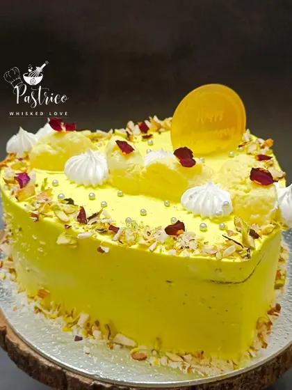 A heart-shaped Rasmalai Cake, perfect for anniversaries and special celebrations. It's adorned with meringue kisses, silver pearls, and dried rose petals for a romantic touch.