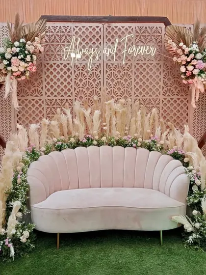 This pastel-themed photo booth features a "Always and Forever" neon sign against a lattice backdrop. The pampas grass and blush pink sofa add a touch of modern, bohemian flair.