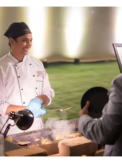 A smiling chef interacting with a guest while serving freshly grilled items from the barbecue.