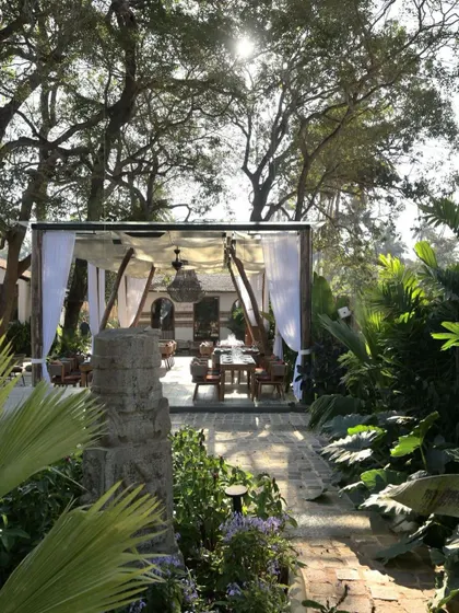 An outdoor dining area at Sanctuary Bar, set under a canopy and draped with white curtains. The space feels light and airy, offering an elegant dining experience surrounded by the lush Goan landscape.