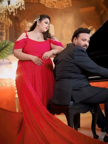 An elegant indoor scene with a grand piano. The off-shoulder red gown adds a touch of classic Hollywood glamour to this sophisticated pre-wedding shoot.